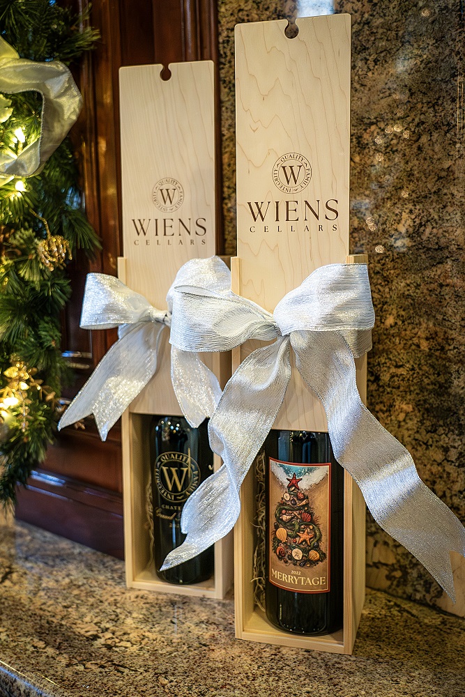 two magnum bottles placed elegantly in their own wooden wine boxes standing up next to eachother each with a silver bow on a marble fireplace